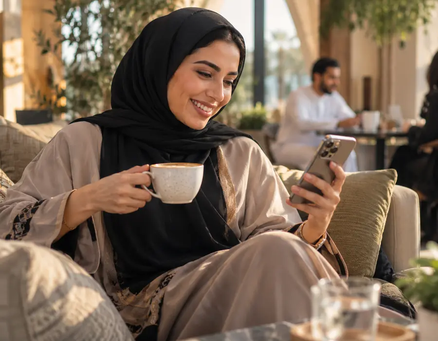 A woman smiling at her phone over coffee